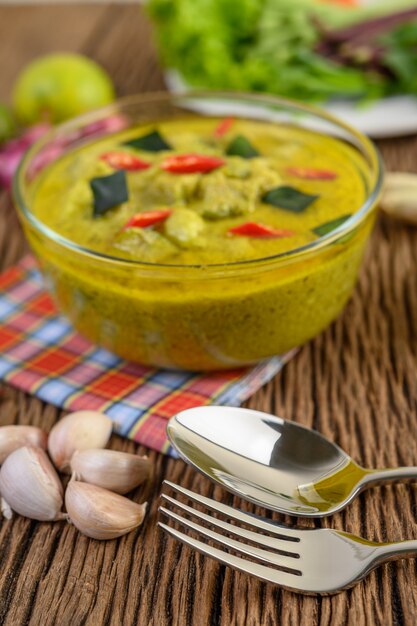 Curry verde en un recipiente con un tenedor y una cuchara en la mesa de madera.