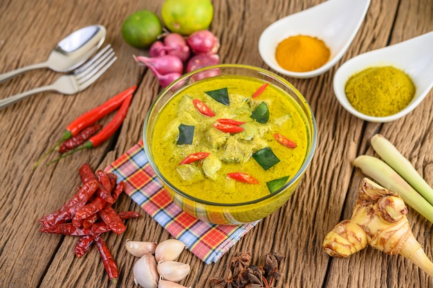 Curry verde en un tazón y especias en mesa de madera.