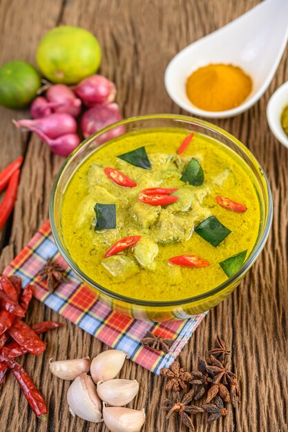 Curry verde en un tazón y especias en mesa de madera.