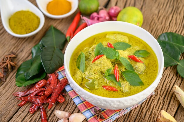 Curry verde en un tazón y especias en mesa de madera.