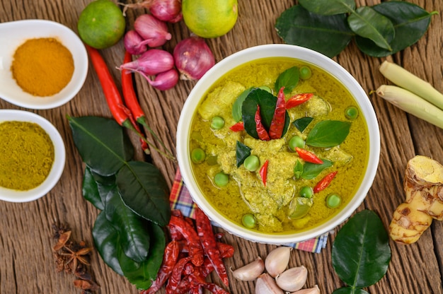 Curry verde en un tazón y especias en mesa de madera.