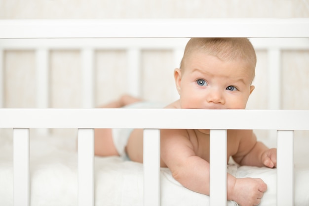 Cute bebé en una cuna chupar la tabla de madera