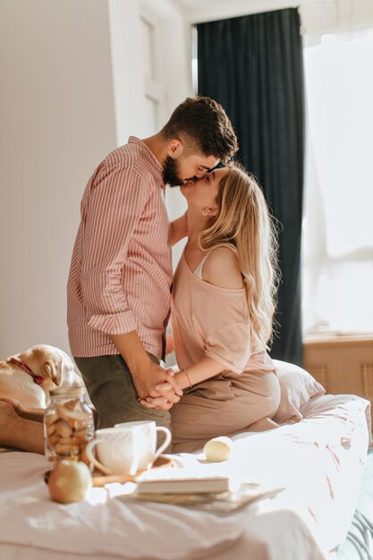 Cute Labrador está acostado en la cama mientras sus amos disfrutan de una hermosa mañana y se besan Instantánea de una pareja romántica en el dormitorio durante el desayuno