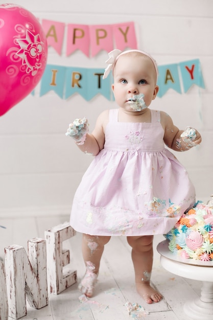 Foto gratuita cute little baby girl vistiendo un vestido rosa ensuciarse en crema para tartas celebrando las vacaciones