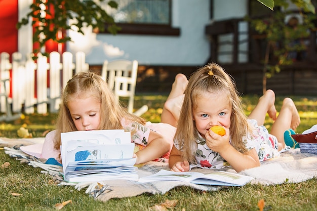 Cute Little Blond Girls leyendo libro afuera sobre la hierba