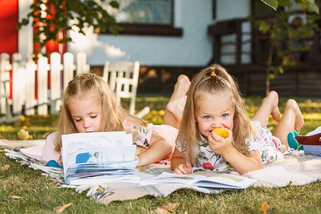 Cute Little Blond Girls leyendo libro afuera sobre la hierba