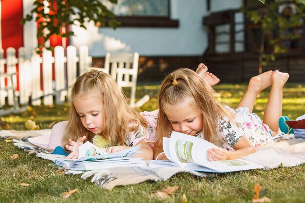 Cute Little Blond Girls leyendo libro afuera sobre la hierba