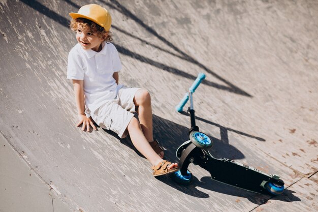 Cute little boy con scooter de pelo rizado