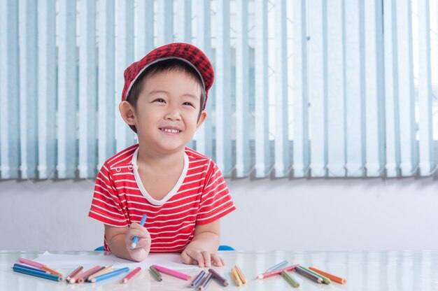 Cute niño dibuja con lápices de colores en la habitación de los niños
