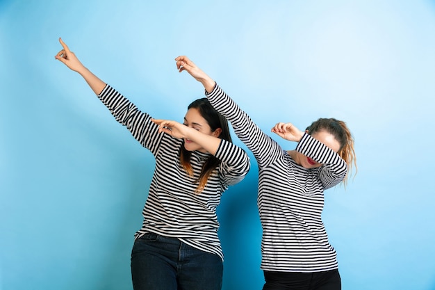 Dabbing. Mujeres emocionales jóvenes aisladas en la pared azul degradado. Concepto de emociones humanas, expresión facial, amistad, anuncio. Hermosas modelos femeninas caucásicas en ropa casual.