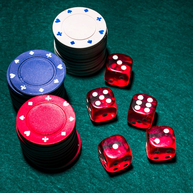 Dados rojos y pilas de fichas de casino en la mesa de póquer verde