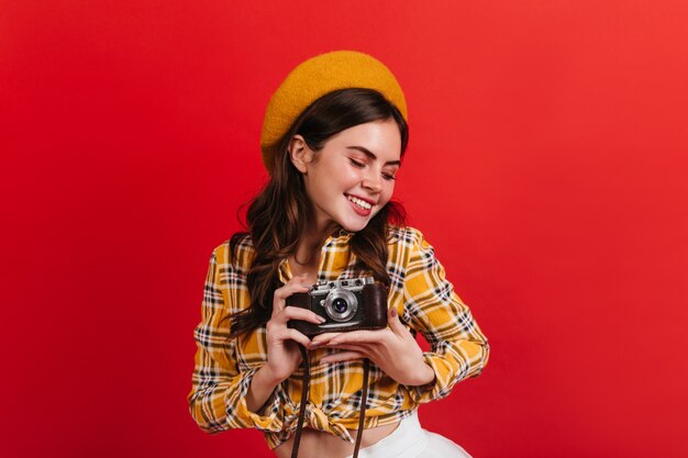 La dama activa es linda sonriendo en la pared roja. Mujer morena toma fotos en cámara retro.