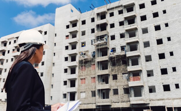 Dama afroamericana en casco de seguridad con papeles cerca del edificio en construcción