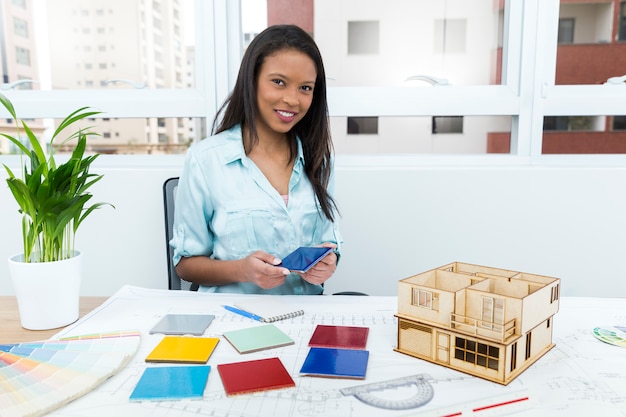 Dama afroamericana en silla con panel de fachada cerca del plano y modelo de casa en mesa