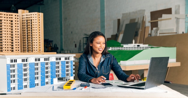 Dama afroamericana sonriente con laptop y modelo de edificio