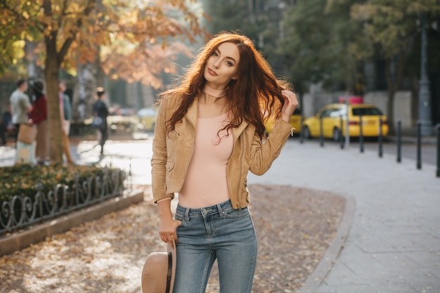 Foto gratuita dama bien formada jugando con su largo cabello rojo en el día de octubre