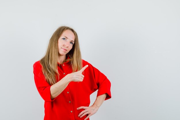 Dama de camisa roja apuntando a la esquina superior derecha y mirando confiada,