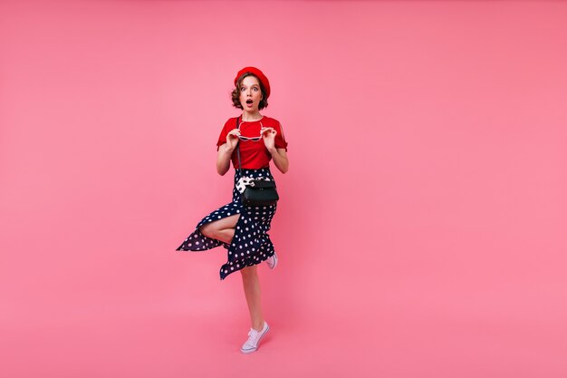 Dama caucásica sorprendida en la presentación de la falda negra de moda. Tiro integral del modelo femenino francés asombrado aislado.