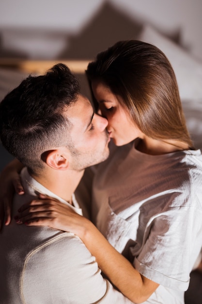 Dama y chico besándose y abrazándose en la cama en un cuarto oscuro