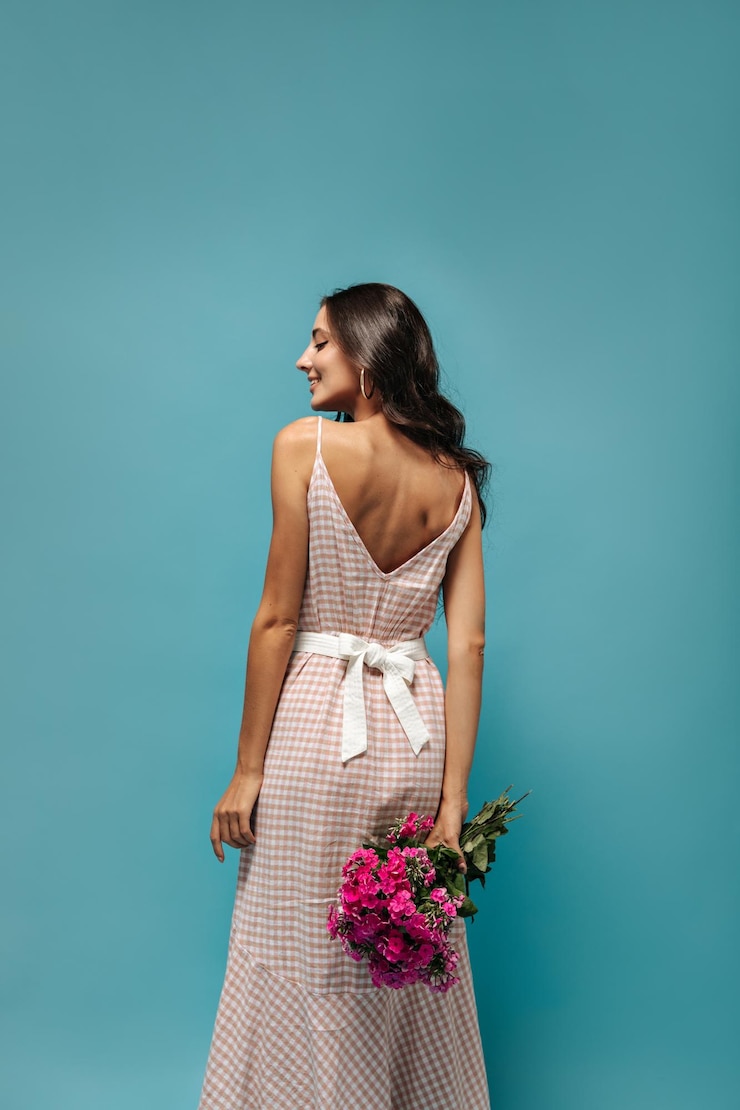 Foto gratuito una dama encantadora con un vestido largo a cuadros de moda con un cinturón ancho blanco posando con un ramo rosa y sonriendo en un fondo aislado