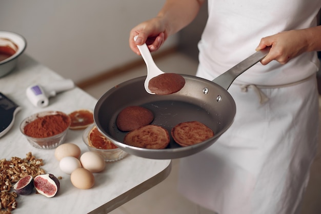 La dama está preparando el postre. Pastelero hornea panqueques. La mujer sostiene una sartén en sus manos.