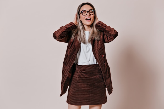 Foto gratuita dama de gafas, camiseta blanca y traje marrón sonriendo en la pared beige