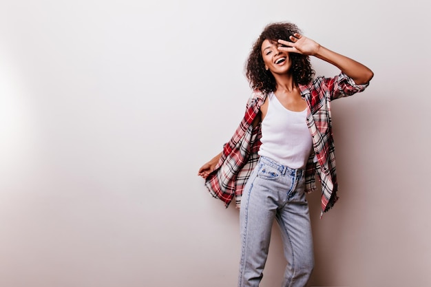 Una dama guapa y despreocupada sonriendo a la cámara Una chica africana tímida con el pelo ondulado disfrutando de una sesión de fotos en interiores