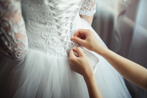 Dama de honor hace nudo de lazo en la parte posterior de las novias vestido de novia