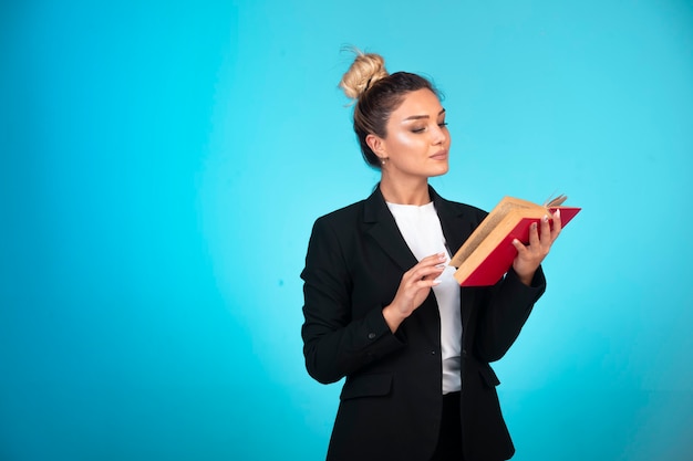 Dama de negocios en chaqueta negra con un libro rojo pensando y leyendo.