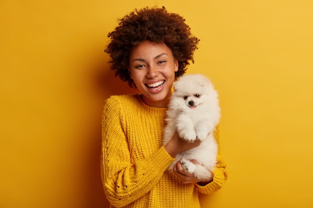 dama de piel oscura mantiene los labios redondeados, quiere besar a una adorable mascota, juega con un pequeño cachorro