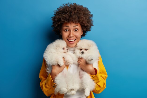 dama de piel oscura mantiene los labios redondeados, quiere besar a una adorable mascota, juega con un pequeño cachorro