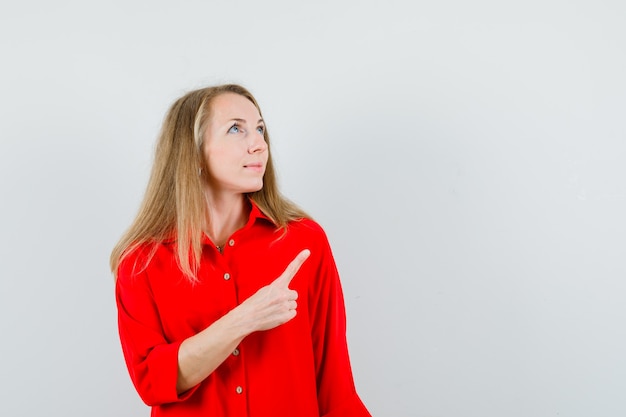 Dama rubia apuntando hacia arriba con camisa roja y luciendo esperanzada,