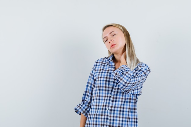 Foto gratuita dama rubia sosteniendo la mano en el cuello con camisa a cuadros y mirando relajado