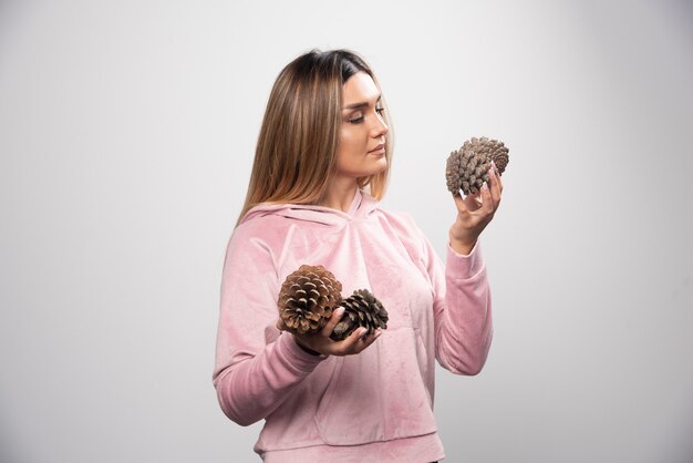 La dama rubia en sudadera rosa hace una cara positiva y feliz sosteniendo conos de roble.