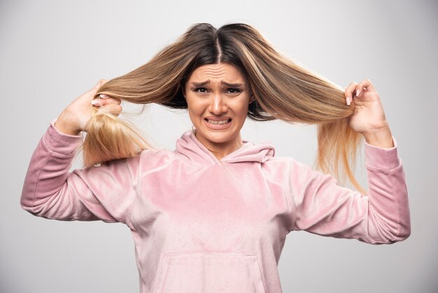 Foto gratuita la dama rubia con sudadera rosa se siente insatisfecha con su cabello seco o con el color del cabello.