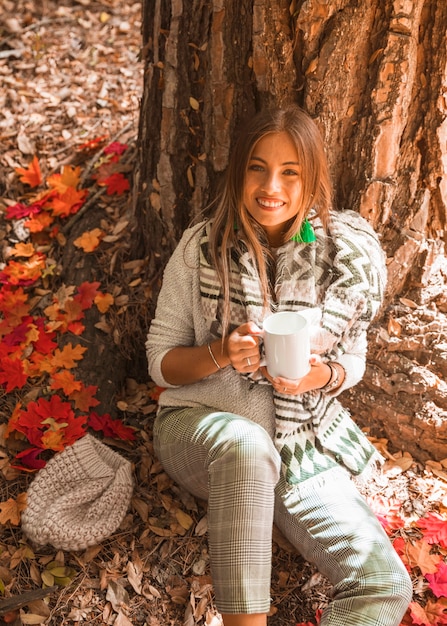 Dama sonriente con bebida en el bosque de otoño