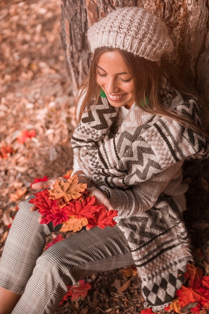 Dama sonriente con hojas sentado cerca de un árbol