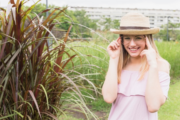 Foto gratuita dama sonriente en lentes y sombrero cerca de hierba alta