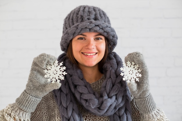 Dama sonriente en mitones, bufanda y sombrero con copos de nieve de adorno en las manos