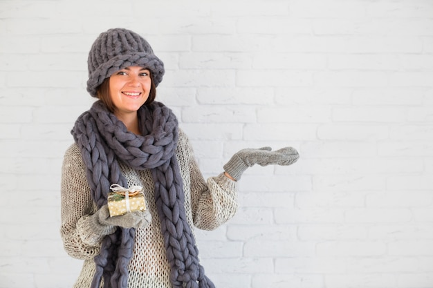 Dama sonriente en mitones, gorro y bufanda con caja actual y mano abierta