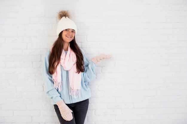 Dama sonriente en mitones, gorro y bufanda con la mano abierta