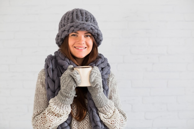 Dama sonriente en mitones, gorro y bufanda con taza en las manos