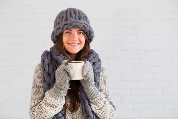 Dama sonriente en mitones, gorro y bufanda con taza en las manos