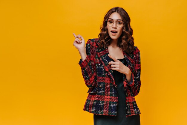 Dama sorprendida con gafas y traje de rayas mostrando el lugar para el texto en una pared aislada