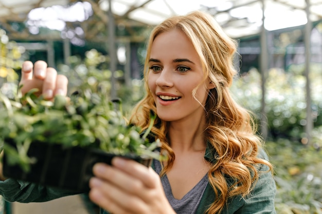 La dama sorprendida de ojos verdes mira la planta con asombro. Retrato de una linda modelo europea de pelo largo que ama la botánica.