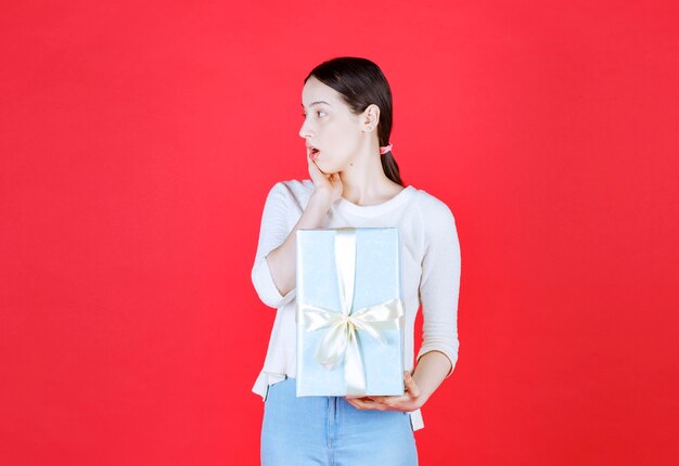 Dama sorprendida sosteniendo caja de regalo y mirando a otro lado