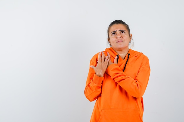 Dama en sudadera con capucha naranja manteniendo las manos en el pecho y mirando preocupada