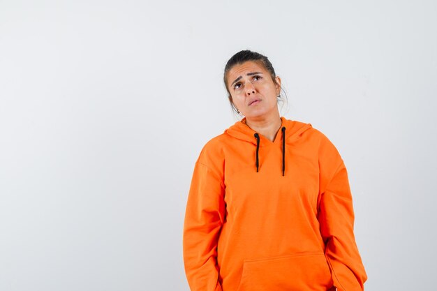 Dama en sudadera con capucha naranja mirando hacia arriba y vacilante