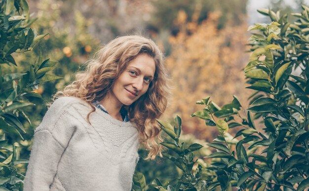 Dama de suéter gris de pie y sonriendo en la naturaleza durante el día