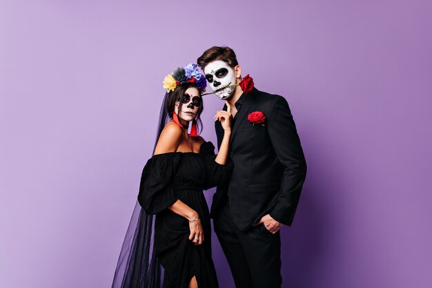 Dama en traje negro posando con su novio. Foto de pareja con maquillaje de Halloween.